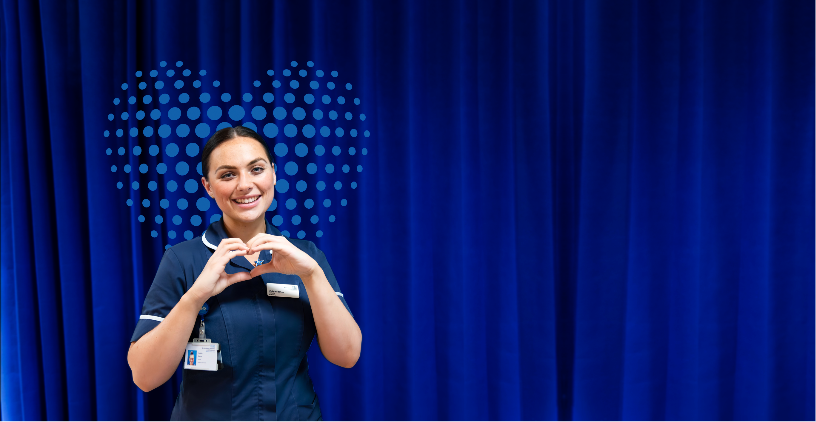 Nurse in-front of a blue curtain doing a heart sign with her hands